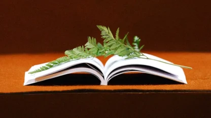 Livro aberto em cima de uma mesa com ramos de folhas posicionados no centro do livro.