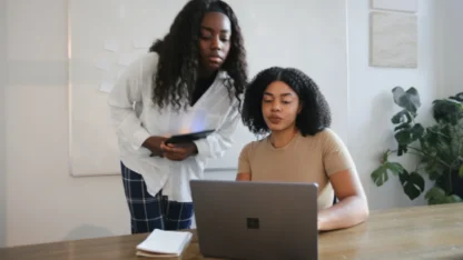 Duas mulheres conversam em frente a um notebook.