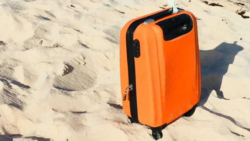 Mala de viagem na cor laranja sobre areia da praia.