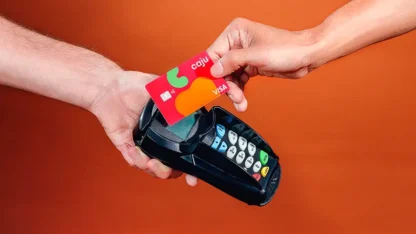 Mão segurando uma máquina de cartão de crédito enquanto a outra mão aproxima um cartão Caju Benefícios.