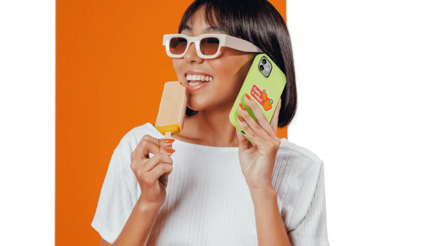 Pessoa com óculos de sol segurando um celular e um picolé.